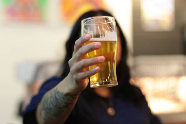 A long-haired person holds a partially full beer glass in front of their face.
