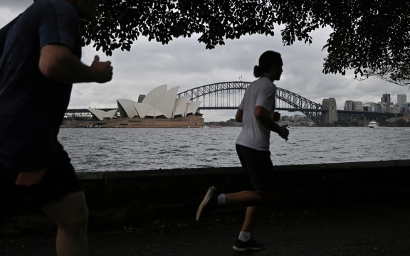 People run before the Opera House and Harbour Bridge in Sydney on December 20, 2020, after authorities introduced a fresh round of restrictions.