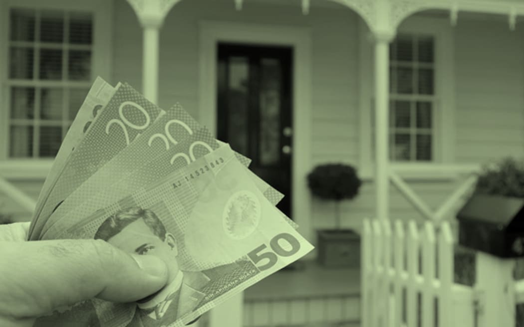 In the foreground of the bottom left corner of the image, a hand holds five New Zealand banknotes. In the background is a wooden home. The image has a green wash over it.