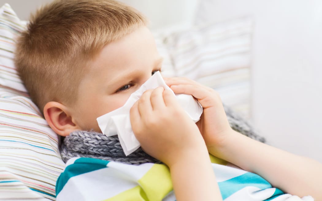 childhood, healthcare and medicine concept - ill boy with flu blowing nose at home
