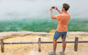 New Zealand travel tourist taking phone picture of famous attraction Champagne pool, Waiotapu.  Rotorua,