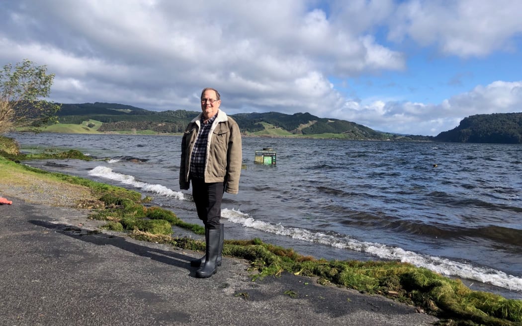 A man stands at the edge of a flooded lake.