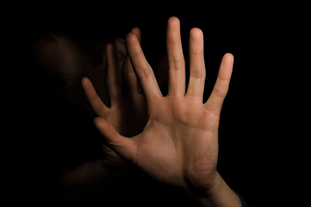 Man putting up hands to hide face (almost obscured in background)