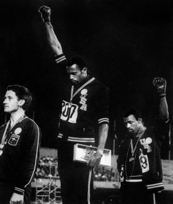 US athletes Tommie Smith, centre, and John Carlos, right, raise their gloved fists in the Black Power salute to express their opposition to racism in the US.