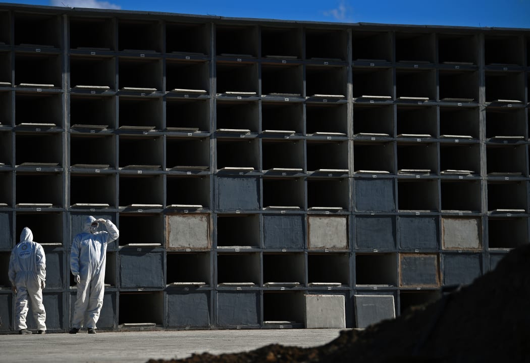 Cemetery workers wearing protective clothing wait by grave cubicles to perform a funeral for a Covid-19 victim in Rio de Janeiro, Brazil