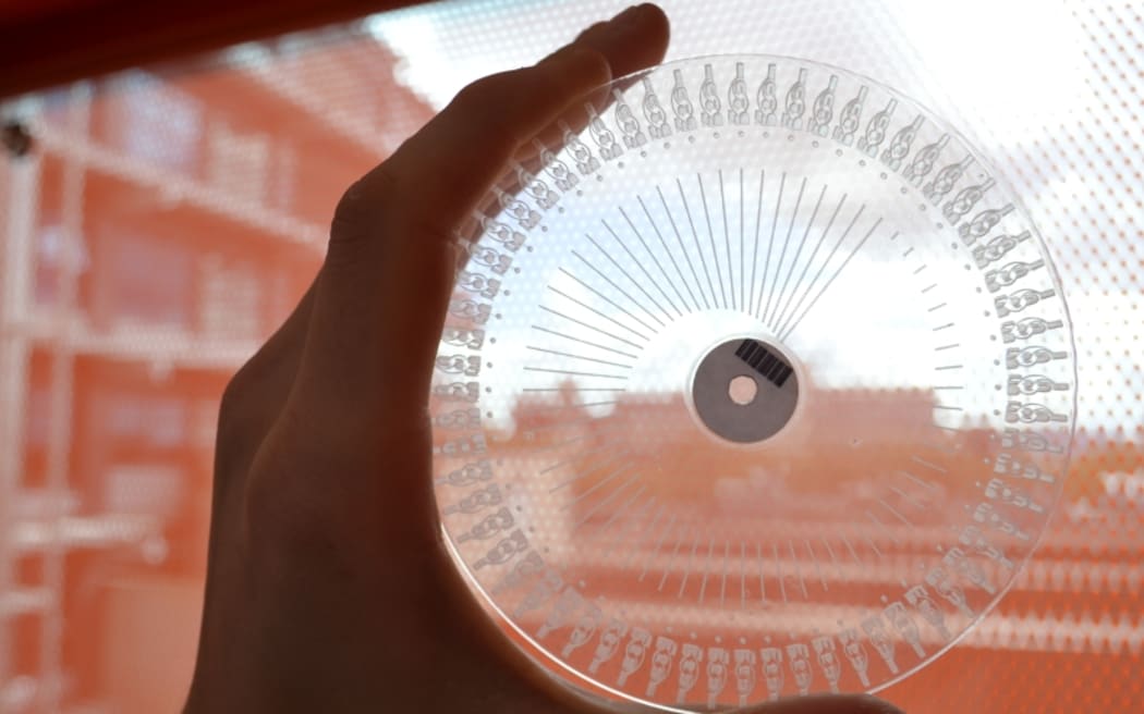 An example of a transparent disc, with carved channels and wells visible, used to analyse milk samples.