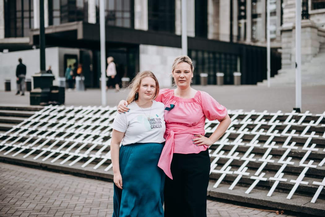 Jane Ludemann and Tash Crosby stand in Parliament grounds in front of 182 white crosses representing the number of people who died of ovarian cancer in 2020.