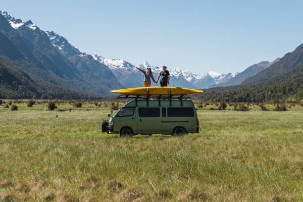 Abigail Hannah and her husband Isaac stand on top of their van in with a mountain scenery backdrop.