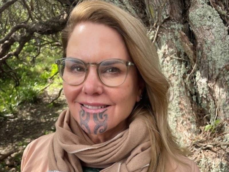 Dr Hinemoa Elder, wearing a brown scarf and brown jacket, holds a copy of her new book Ara.