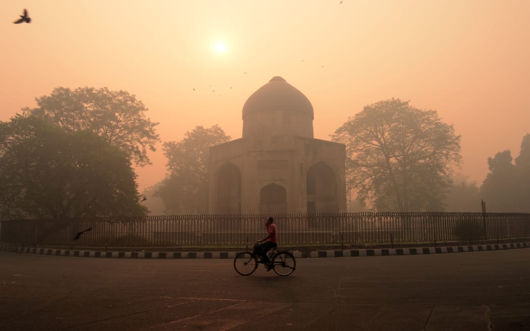 An Indian cyclist rides along a street as smog envelops a monument in New Delhi, the day after the Diwali festival.