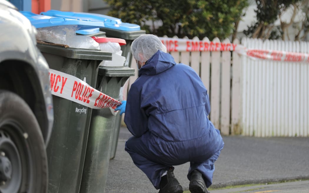 A police investigator looks closely at a set of rubbish bins on Renall St
