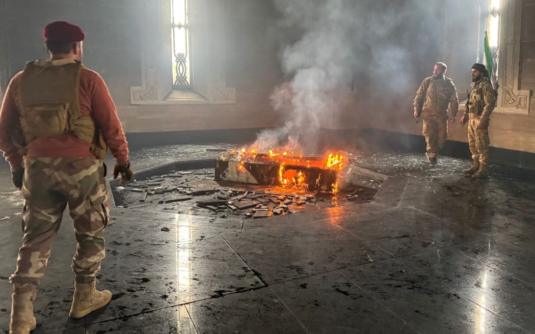 Rebel fighters standing next to the burning gravesite of Syria's late president Hafez al-Assad at his mausoleum in Latakia province, after it was stormed by opposition factions.