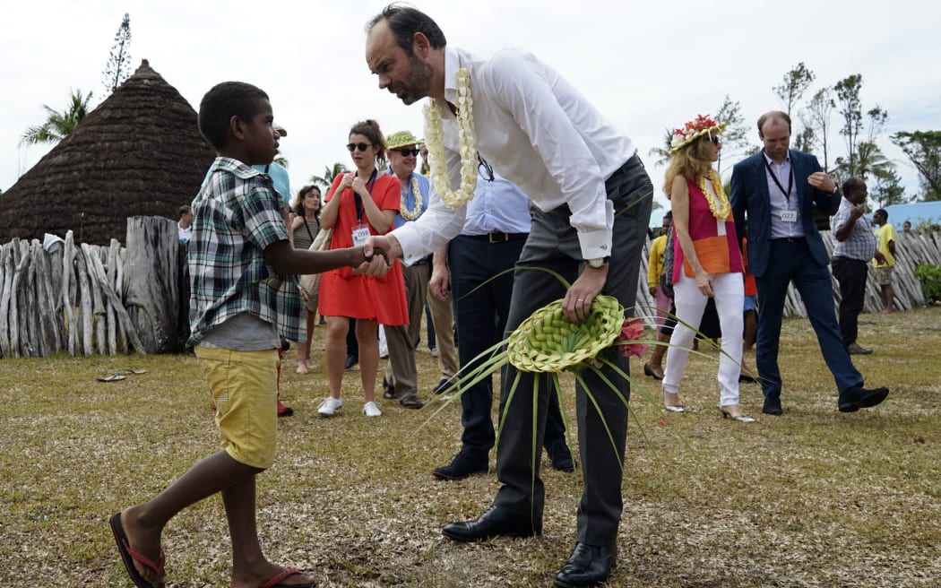 French Prime Minister Edouard Philippe (R), shakes hands with a child during welcoming ceremony at the Grande Case in the district of Wetr, in Hnatalo, on the Lifou Island, during his visit to the French overseas territory of New Caledonia on December 3, 2017. / AFP PHOTO / Fred Payet