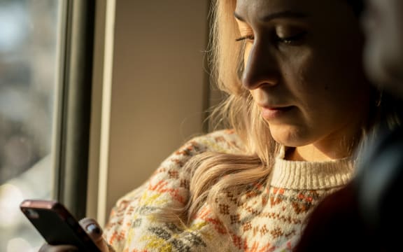 A blonde woman in soft light looks down at her phone.