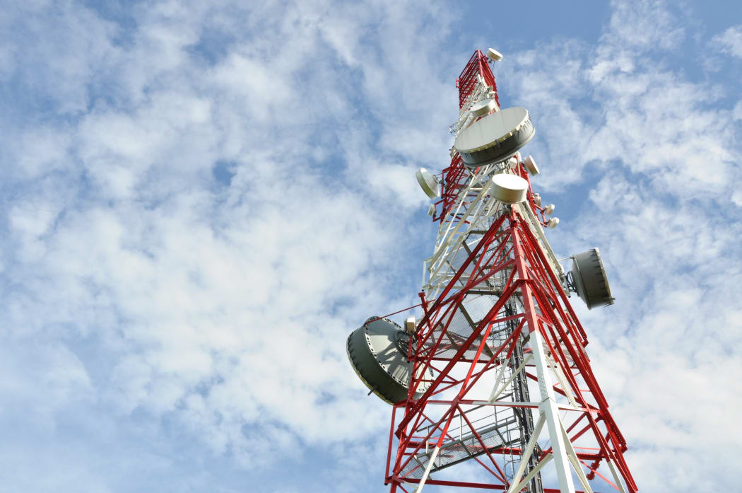 Tower with cell phone antenna system against blue sky.