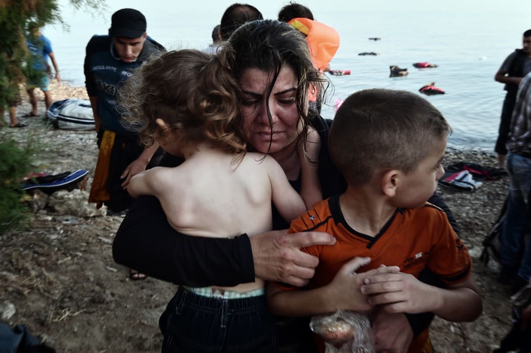 A Syrian woman holds her children as they arrive on an overcrowded dinghy on a beach near the port on the Greek island of Kos on 15 August.