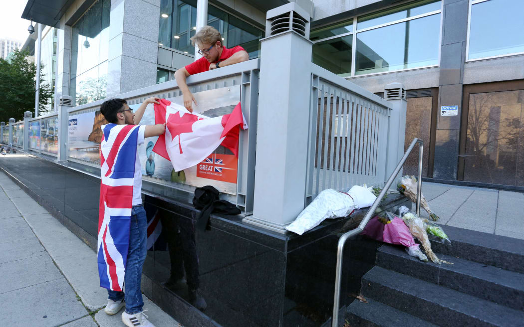 Mourner Eissa Saddozai (L) and Aidan Osadchuk place a Canadian flag on the front steps of the British High Commission after the death of Britian's Queen Elizabeth II September 9, 2022 in Ottawa, Canada.