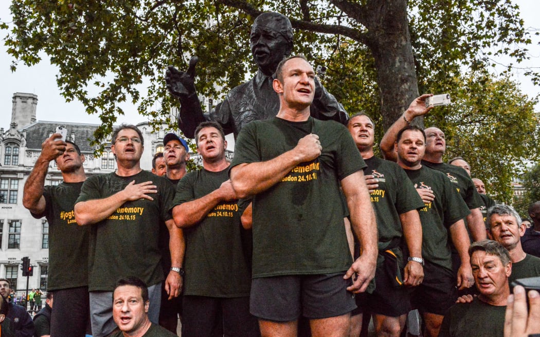 Captain Francois Pienaar and the 1995 South African Rugby World Cup winning squad lead fans in a rendition of their national anthem by a statue of Nelson Mandela in Parliament Square during a run through the capital early on October 24, 2015 in London, England.