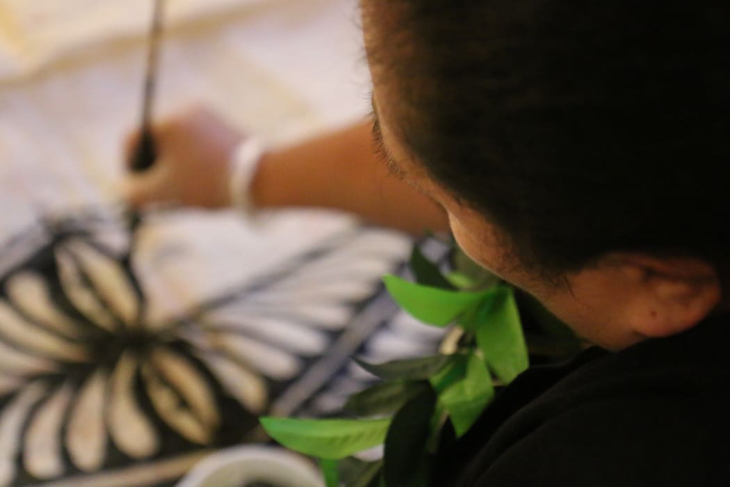 Steady hands  in the final stages of Tongan ngatu making, adorning the ngatu with intricate Tongan symbols and designs.