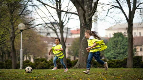 Children wearing hi-vis, running on field, kicking a soccer ball.