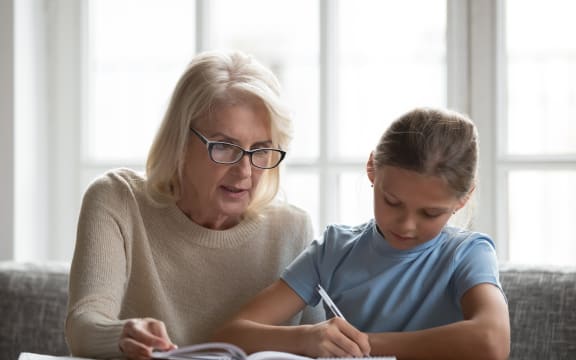 Middle-aged private tutor in glasses helping schoolchild with homework.