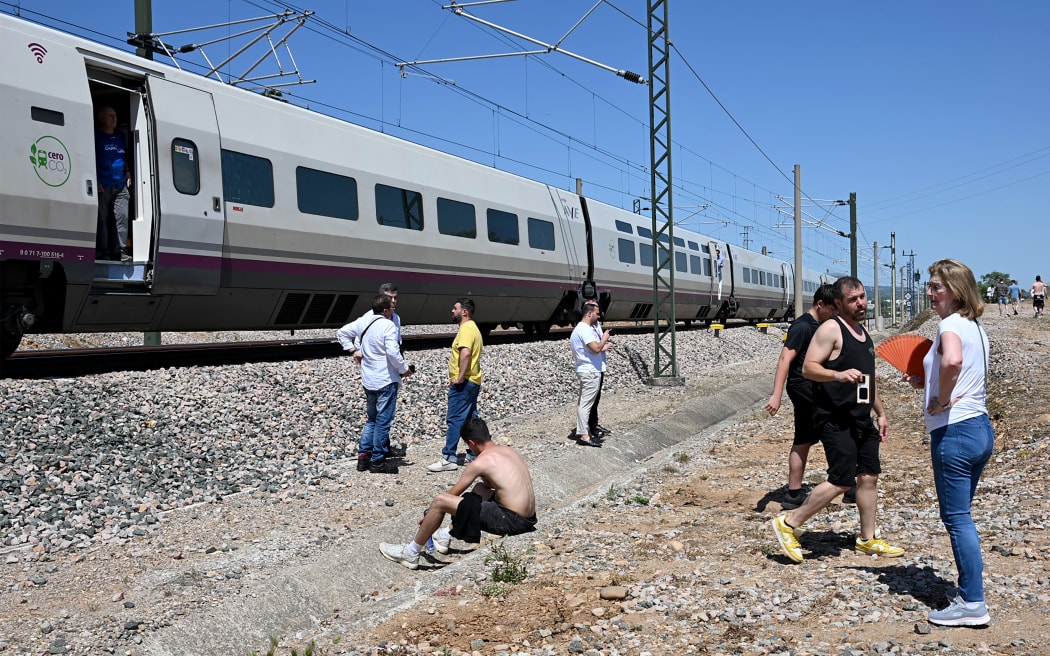Passengers stand next to a stopped high-speed AVE train near Cordoba on April 28, 2025, during a massive power cut affecting the entire Iberian peninsula and the south of France. A "massive" power cut late on April 28, 2025 morning affected the whole of the Iberian peninsula and part of France, according to Portuguese electricity network operator REN. (Photo by JAVIER SORIANO / AFP)