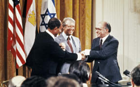 Egyptian President Anwar al-Sadat (L), Israeli Premier Menachem Begin (R) and US President Jimmy Carter (C) shake hands after a press conference in the East Room of the White House, on September 17, 1978. Egypt began peace initiatives with Israel in late 1977. A year later, with the help of Carter, terms of peace between Egypt and Israel were negotiated at Camp David. A formal treaty, signed 26 March 1979 in Washington, D.C., granted full recognition of Israel by Egypt, opened trade relations between the two counties, and limited Egyptian military buildup in the Sinai. Israel agreed to return to final portion of occupied Sinai to Egypt. (Photo by CONSOLIDATED NEWS / AFP)