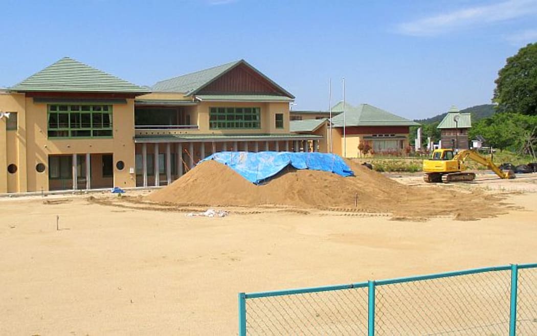 2 storey school buildings with a digger and pies of dusty earth in front