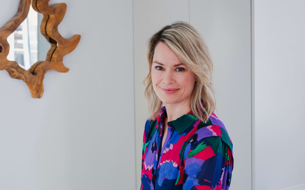 Gretchen Lowe stands at a table with dishes of food. She is wearing a brightly coloured red, blue and purple dress.