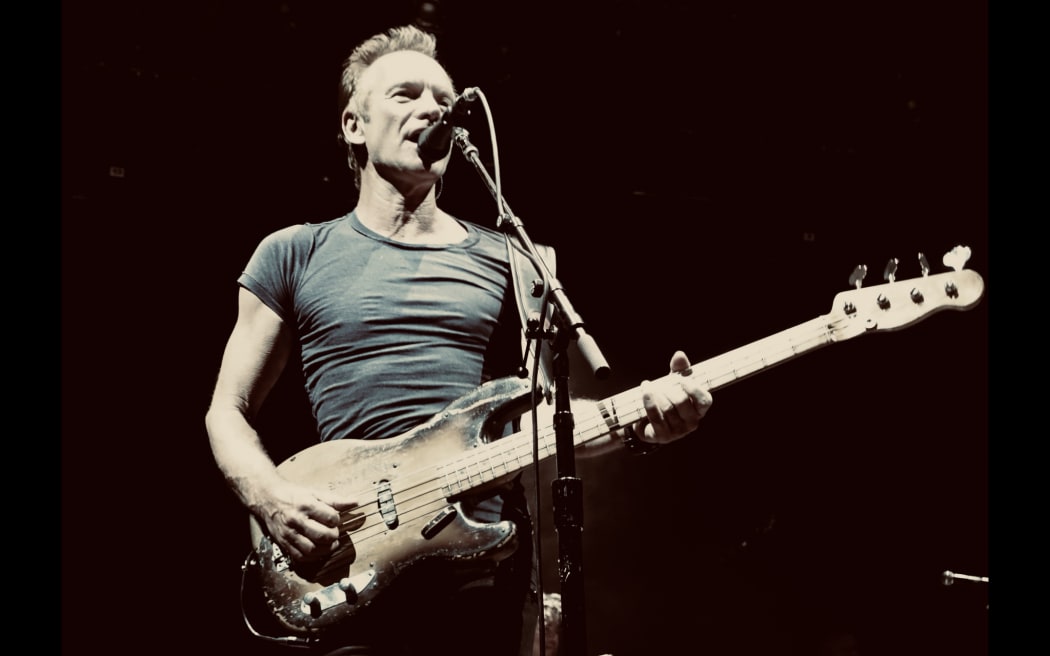 Sting holds a guitar while performing on stage.