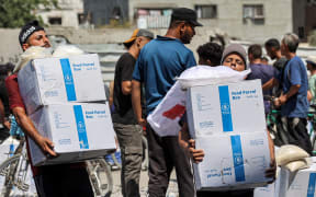 People receive humanitarian aid packages provided by the United Nations Relief and Works Agency for Palestine Refugees (UNRWA) from a warehouse in central Gaza City on August 27, 2024 amid the ongoing conflict in the Palestinian territory between Israel and Hamas. (Photo by Omar AL-QATTAA / AFP)