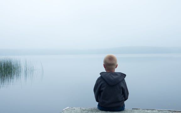 47556115 - sad child sitting alone by lake in a foggy day, back view