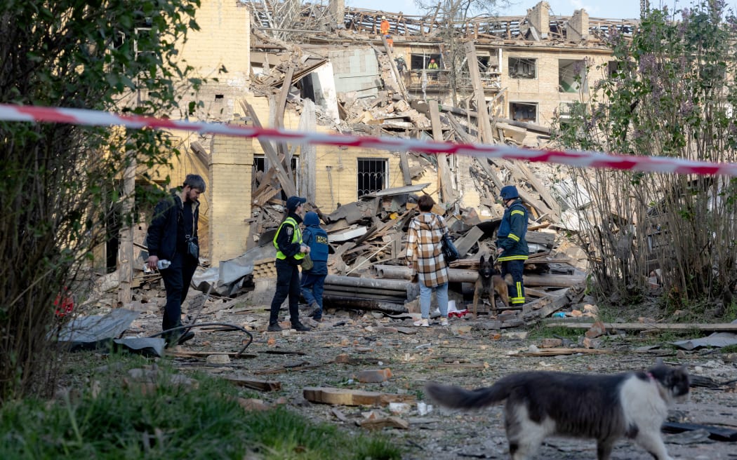 Police officers and local residents stand next to damaged apartment buildings following a Russian missile attack in Kyiv on April 24, 2025, amid the Russian invasion of Ukraine. A "massive" Russian missile attack on Kyiv on April 24, 2025, killed at least nine and wounded dozens in one of the deadliest strikes on the Ukrainian capital since Moscow launched its invasion more than three years ago. (Photo by Tetiana DZHAFAROVA / AFP)