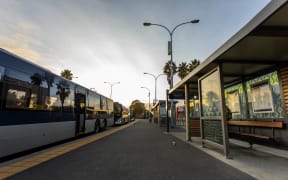 The bus station in Mangere. One man is seen waiting in the bus stop. The rest of the area is quiet.