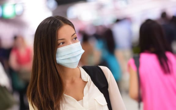 Person wearing protective mask against transmissible infectious diseases and as protection against pollution and the flu. Asian woman commuter in airport public area.