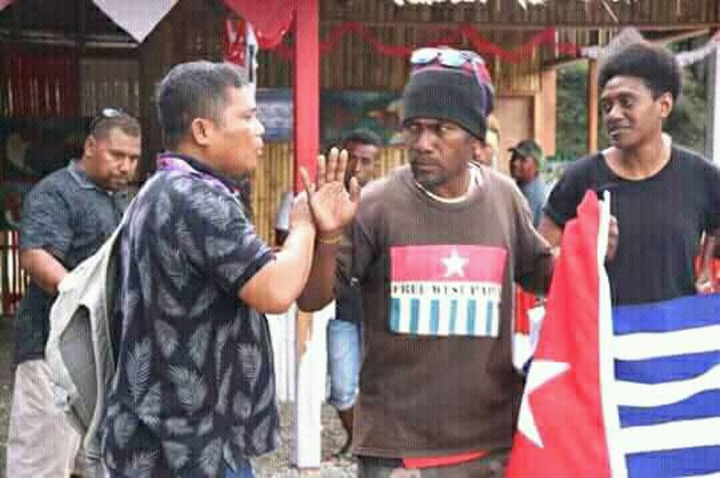 Ben Didiomea displays the West Papuan flag as Indonesian staff try  to usher him away.