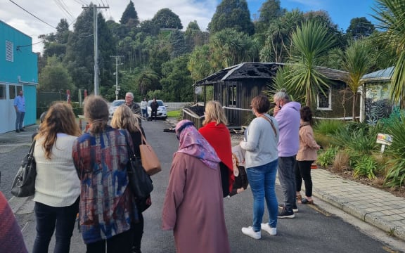 People stand around in the street outside the building as a press conference is given.