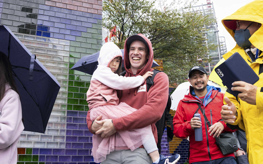 American climber Alex Honnold leaves the scene, in the rain, carrying a young girl in his arms, Taipei, Taipei City, Taiwan, January 24, 2026. 
His planned rope free climb of Taipei 101, scheduled for a live Netflix broadcast, was postponed because of bad weather and he will return the next day. (Photo by Jimmy Beunardeau / Hans Lucas via AFP)