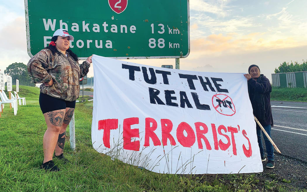 Talei Bryant (L) and another woman work to hang a hand-painted sheet over a road sign outside Te Uru Taumatua offices in Tāneatua.