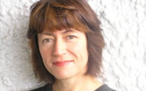 Jennie Miller is wearing a black top and standing in front of a wall. It's a head and shoulders shot.