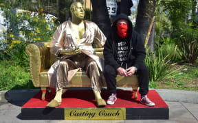 Artist Plastic Jesus poses with the gold sculpture of Harvey Weinstein on his infamous casting couch.
