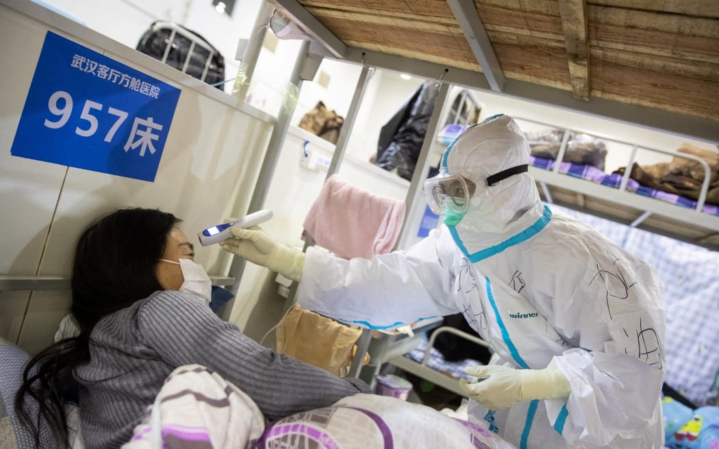 A medic in China checking the body temperature of a patient with symptoms of Covid-19 at a Wuhan exhibition centre converted into a hospital on 17 February, 2020.
