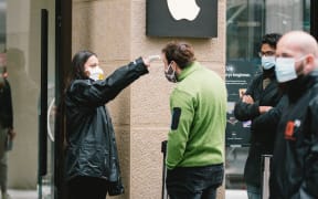 A staff member checks the body temperature of a customer before entering the Apple store in Cologne, Germany