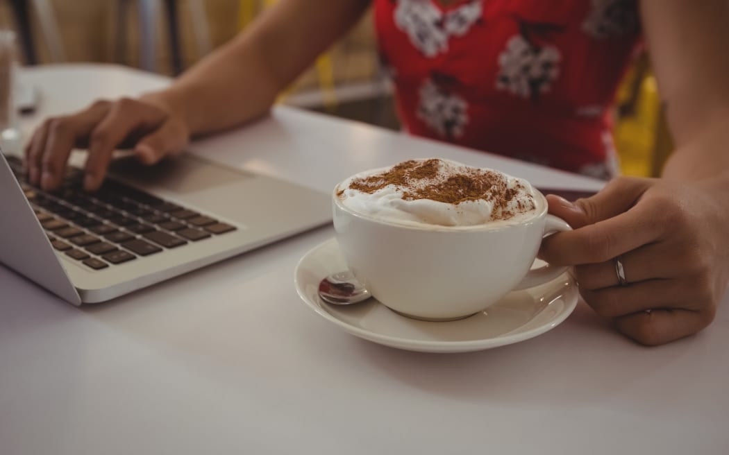 Midsection of woman with coffee using laptop at table in cafe
