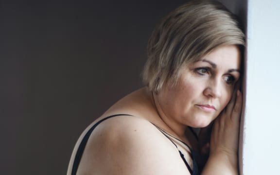 A sad white woman leans against a wall