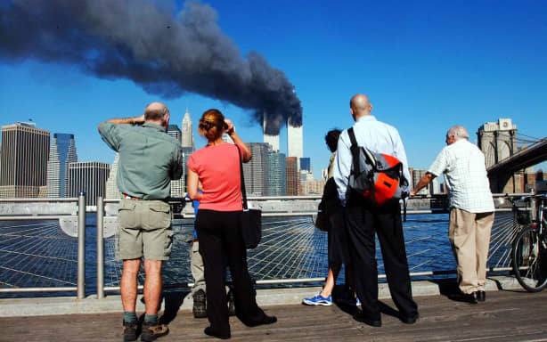 (FILES) In this file photo pedestrians standing on the Brooklyn waterfront look across the East River towards the burning twin towers of the World Trade Center in lower Manhattan, New York on September 11, 2001. On the morning of September 11, 2001, New Yorkers woke to crisp blue skies following a storm that had soaked America's northeastern seaboard the day before. The cloudless, beautiful sky was little portent of the dark, history-changing day that was to come but would remain etched on the memory of those involved. (Photo by HENNY RAY ABRAMS / AFP)