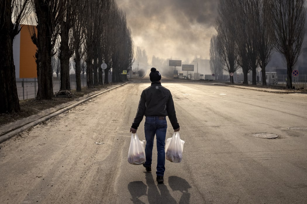 A man walks holding bags near a burning warehouse hit by a Russian shell in the suburbs of Kyiv on 24 March,