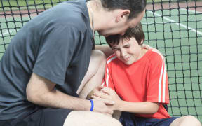 A photo of a father consoling upset boy who has been playing tennis