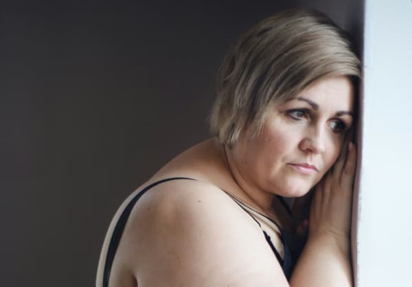 A sad white woman leans against a wall