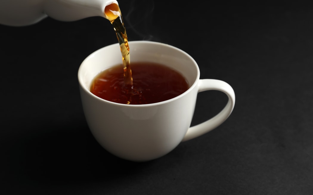 Pouring hot tea into white porcelain cup on dark background